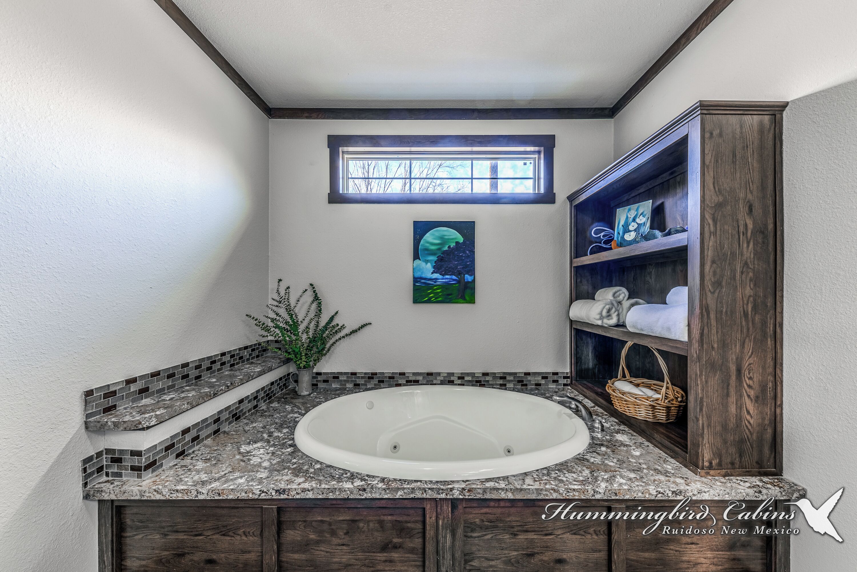 A bathroom with a freestanding bathtub, a window with a view of trees, and a shelf with towels and a basket.