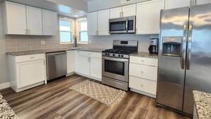 A modern kitchen with white cabinets, stainless steel appliances, a microwave, stove, and refrigerator. - Dunes Forest Retreat (Gary)