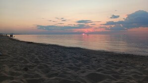 A beach with sand and water, a sunset in the background, and a few people walking. - Dunes Forest Retreat (Gary)
