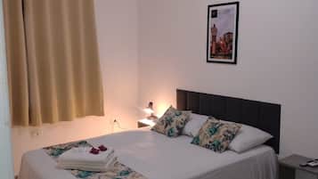 Una cama bien hecha con ropa de cama floral, una mesita de noche con una lámpara y un cuadro en la pared.