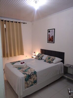 A neatly made bed with floral bedding, a nightstand with a lamp, and a framed picture on the wall. - Brisa Pousada (Gramado)