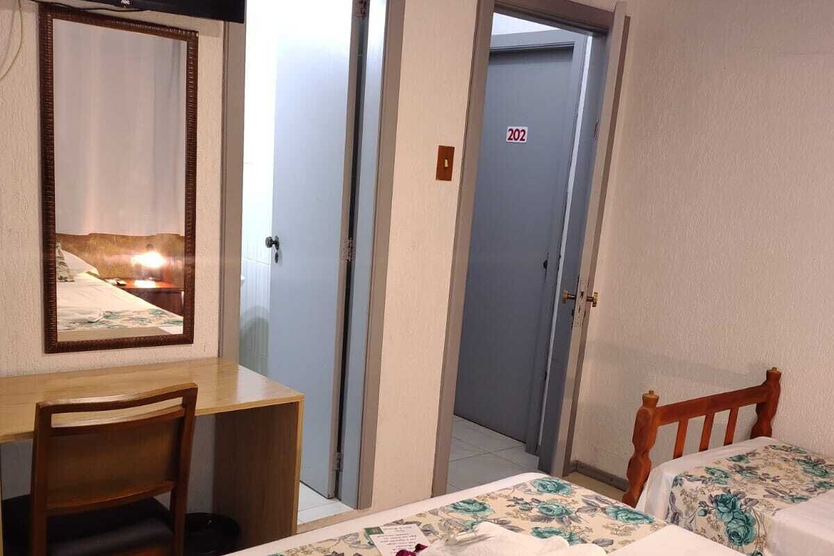 A hotel room with a desk, two beds, a mirror, and a door marked with the number 202.