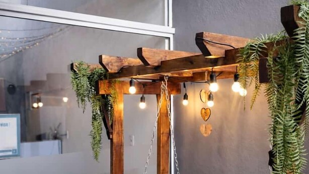 A cozy room with a wooden swing chair, a small table, and a hanging light fixture. - Brisa Pousada (Gramado)