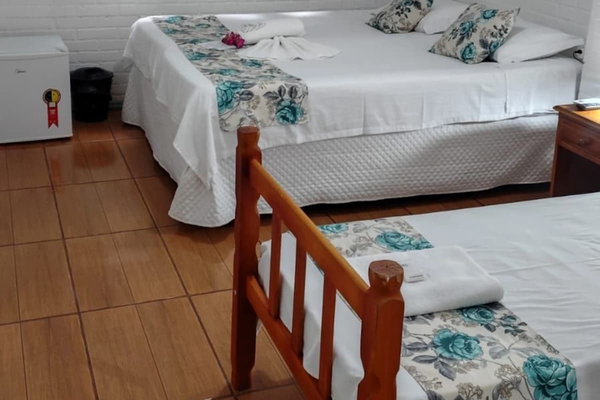 A room with two beds, a wooden chair, a small table, an air conditioner, and a picture on the wall.
