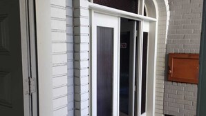 A room with a white brick wall, a sliding glass door, and a small wooden door. - Brisa Pousada (Gramado)