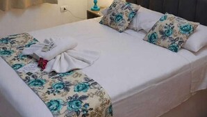 A double bed with floral bedding, a nightstand with a lamp, a framed picture on the wall, and a window with curtains. - Brisa Pousada (Gramado)