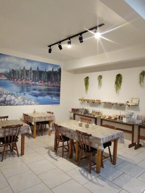 A dining area with tables and chairs, a large painting on the wall, and a kitchen counter with various items. - Brisa Pousada (Gramado)