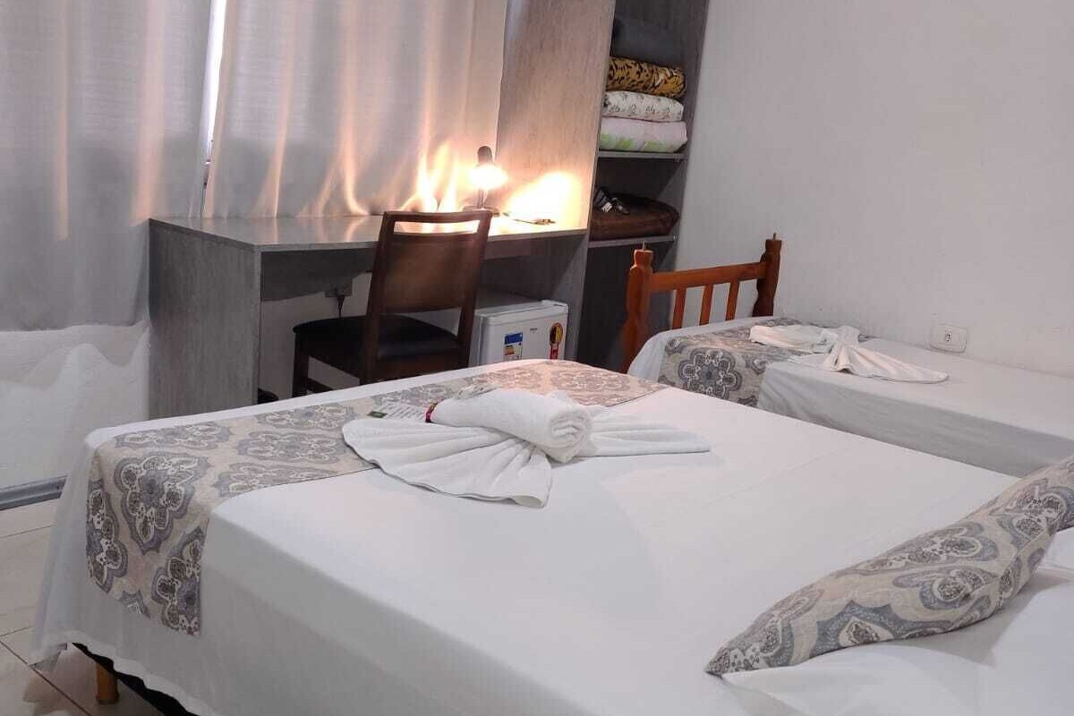 A hotel room with two beds, a desk, a chair, an air conditioning unit, and a window with curtains.