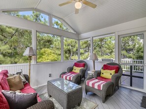 A covered outdoor seating area with wicker furniture and a glass coffee table.