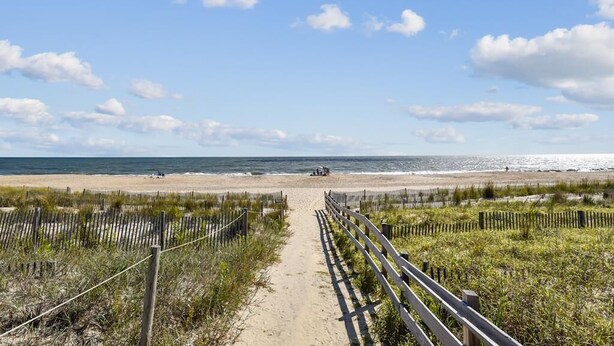 A beach path leading to the ocean with a wooden fence on both sides.