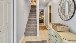 A hallway with a carpeted staircase, a mirror, and a dresser with baskets.