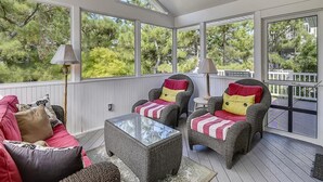 A covered porch with wicker furniture, a glass table, and a ceiling fan.