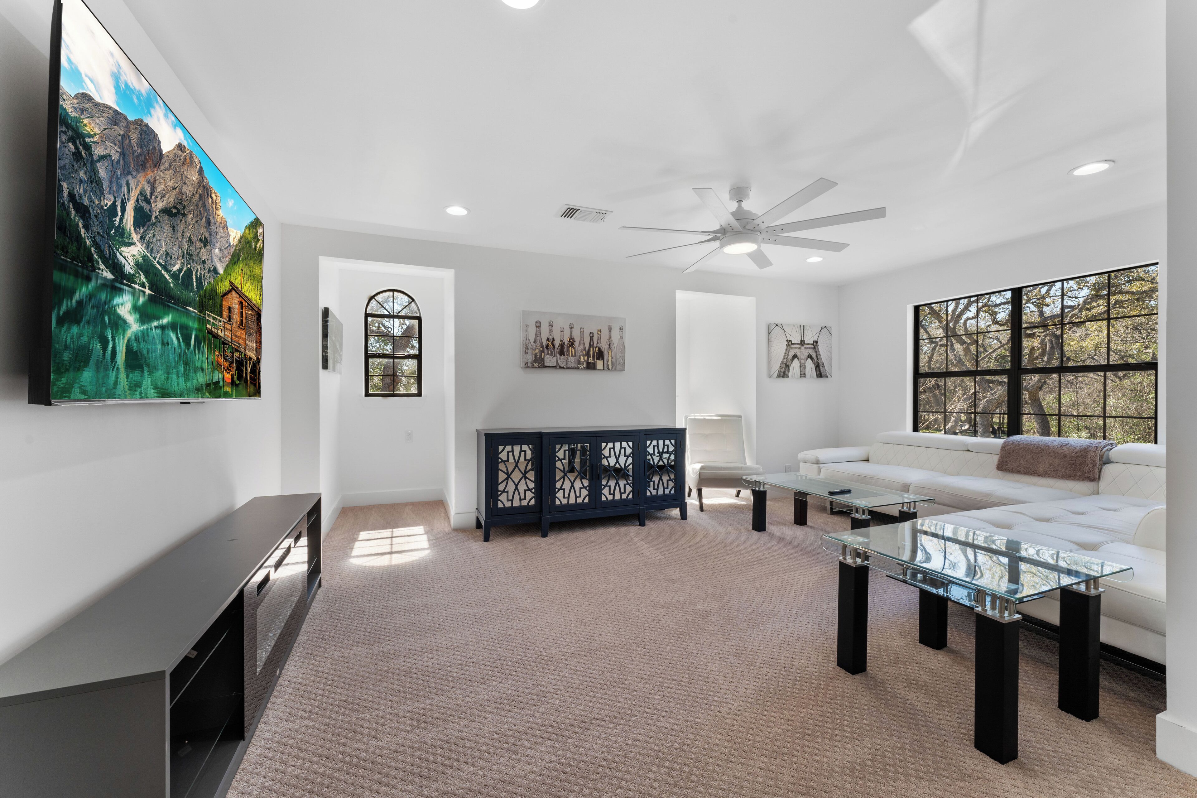 A modern living room with a large flat-screen TV, a glass coffee table, a white sofa, and a dark wooden cabinet.