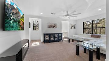 A modern living room with a large flat-screen TV, a glass coffee table, a white sofa, and a dark wooden cabinet.