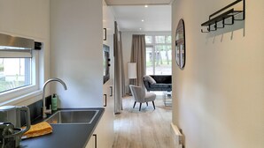 A modern kitchen with a sink, a kettle, and a coffee maker. There is a chair and a table in the adjacent living area.
