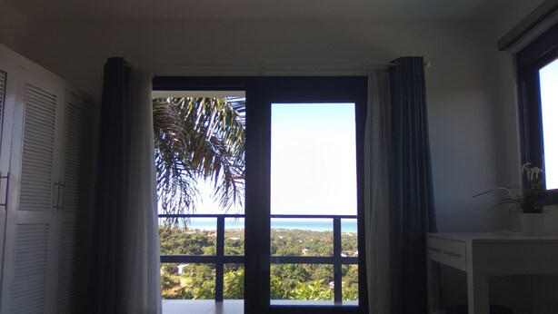 A hotel room with a large window offering a view of a balcony and greenery.