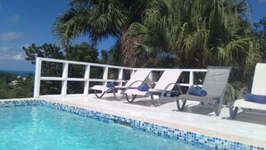 A poolside area with lounge chairs and a view of the ocean.