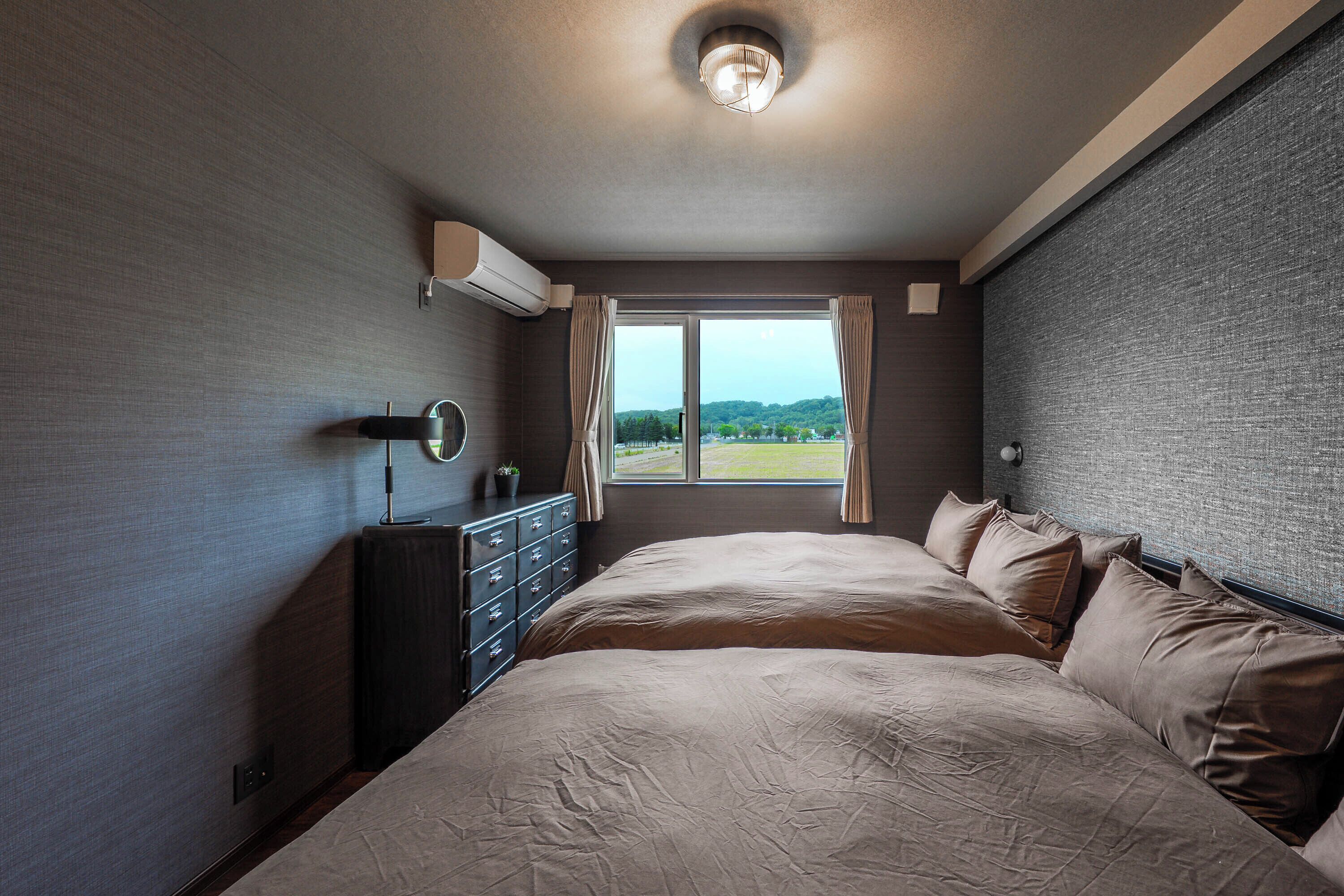 Une chambre à coucher avec un grand lit, une commode, un miroir et une fenêtre avec des rideaux.