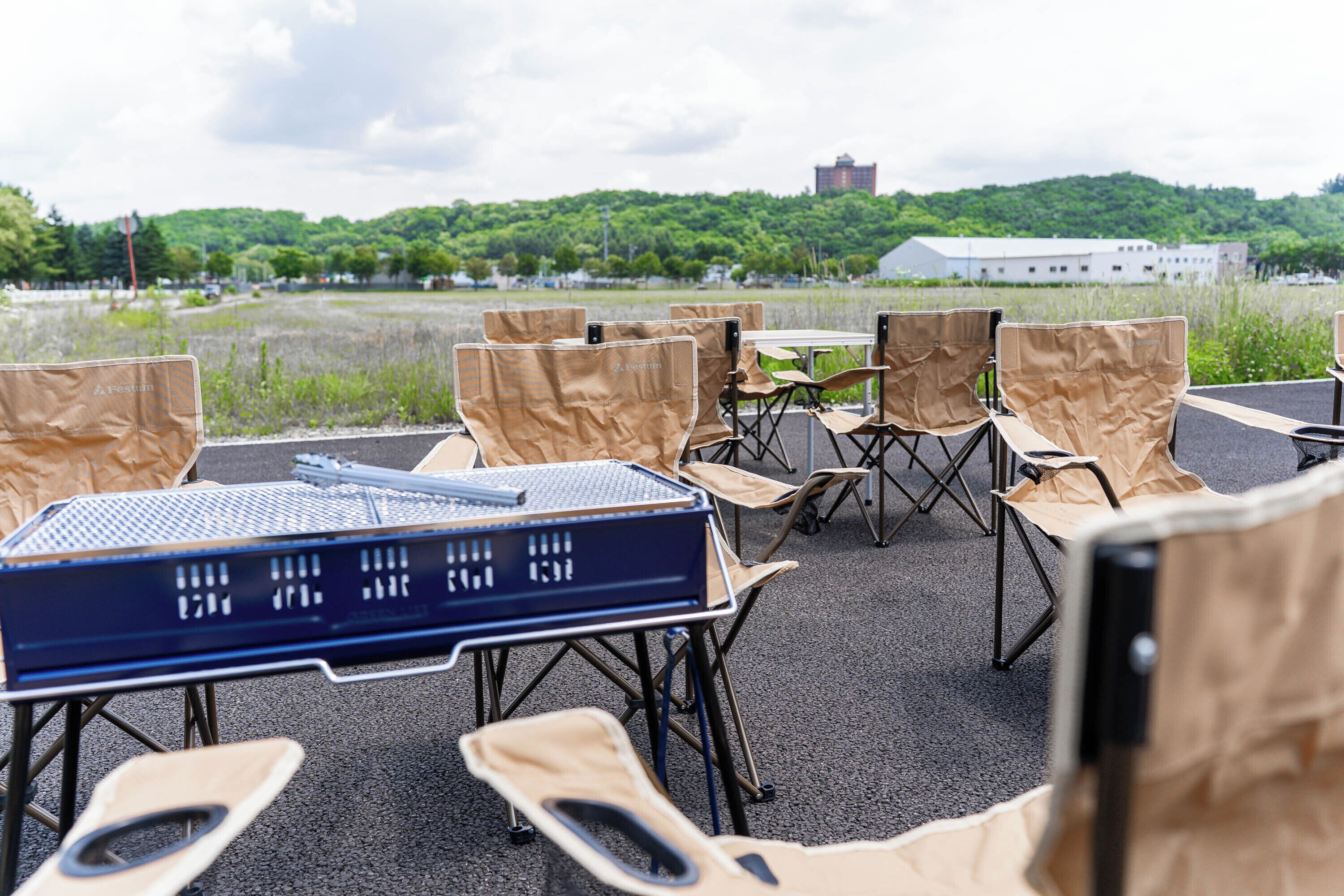 An outdoor seating area with folding chairs and tables, overlooking a green landscape with a building in the distance.
