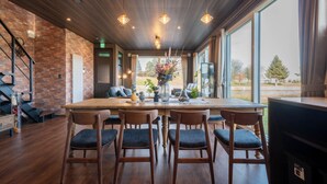 A dining area with a wooden table, four chairs, and a vase of flowers. There is a staircase on the left and a large window on the right. - THE HORIZON RESIDENCE (Makubetsu)