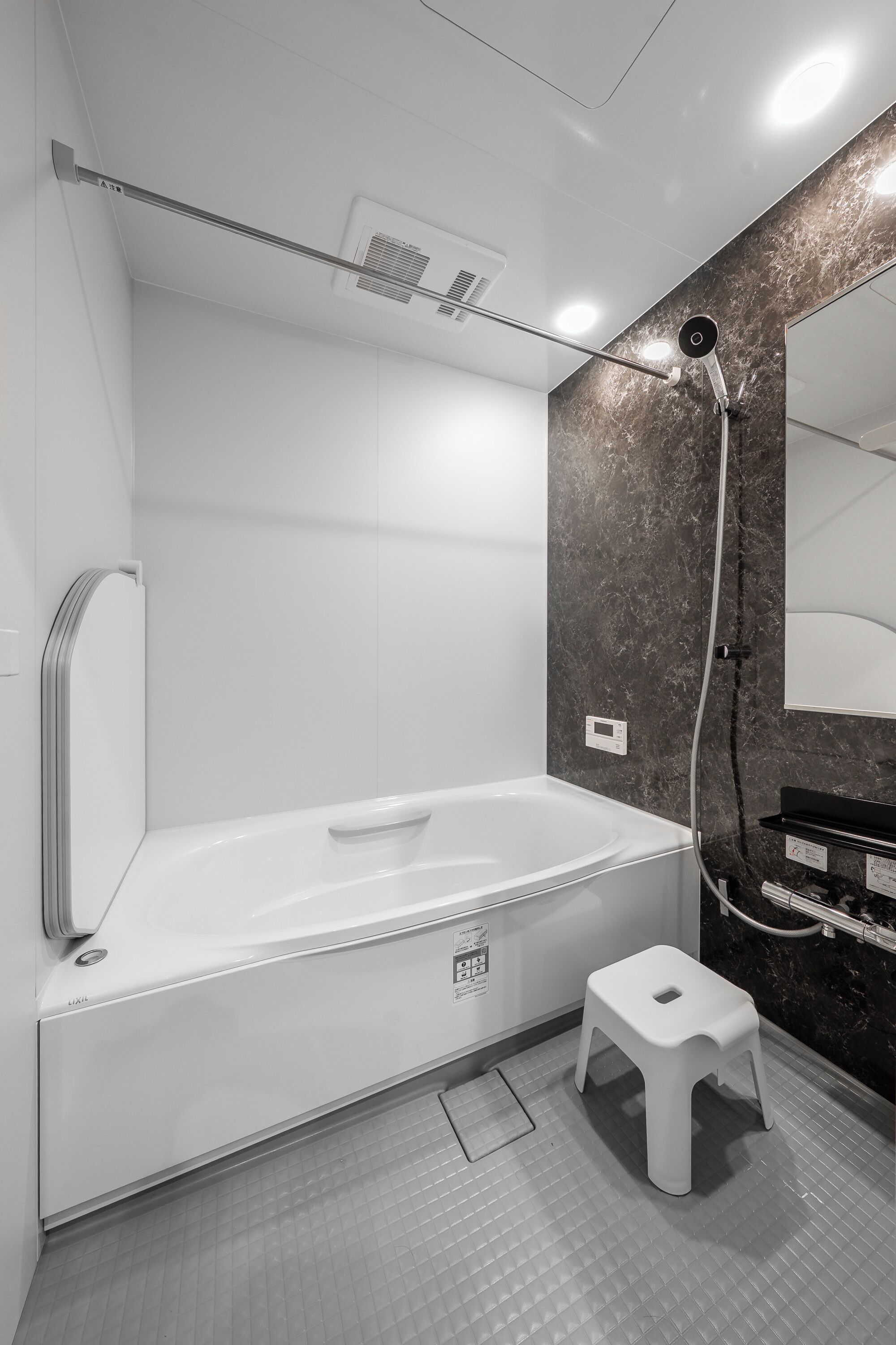 Une salle de bain moderne avec une baignoire blanche, un petit tabouret blanc et un mur en marbre.