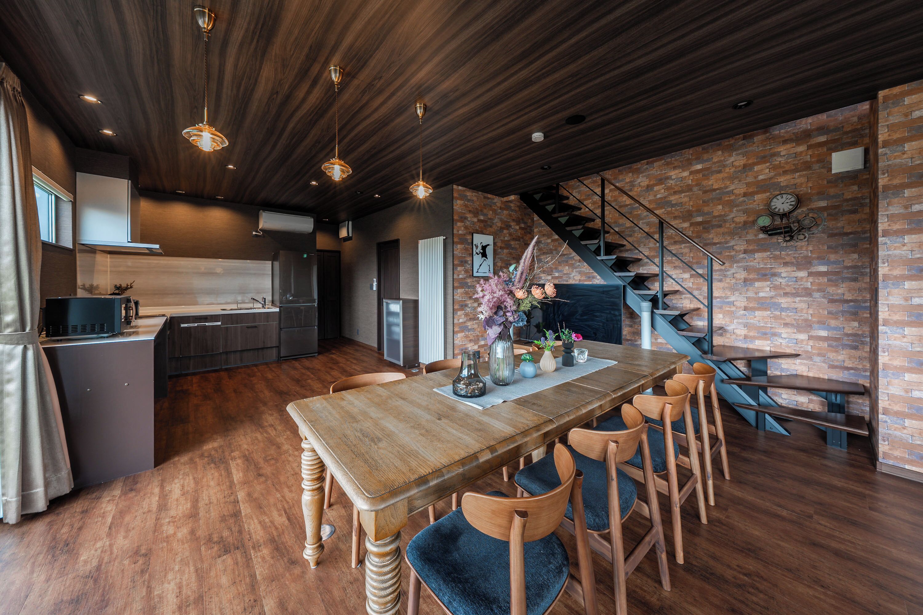 Eine moderne Küche mit Holztisch und Stühlen, einer Ziegelwand und einer Treppe.