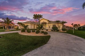A residential house with a driveway, palm trees, and a well-maintained lawn. - Gulf Access, Dock with Tiki, Heated Pool & Pool Table - Mango Paradise-Roelens (Cape Coral)