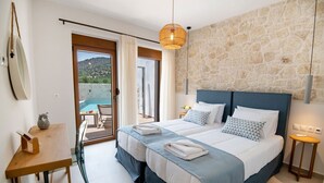 A bedroom with two beds, a stone wall, a wooden table, and a view of the outdoors.