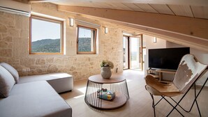 A cozy loft bedroom with a stone wall, a large TV, a round coffee table, and a comfortable seating area.