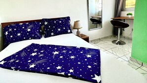A hotel room with a bed, a nightstand, a lamp, a mirror, a window with curtains, and a small plant. - Studio B4 Fustel City, Bonamoussadi Santa Lucia, WiFi, canal, well, janitor  (Douala)