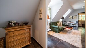 Ein Zimmer mit einem hölzernen Schminktisch, einem grünen Sofa und einem Esstisch mit Stühlen. Über dem Sofa befindet sich ein Oberlicht.