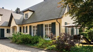 Ein traditionelles Haus mit einem gepflasterten Innenhof, grünen Fensterläden und einem gepflegten Garten.