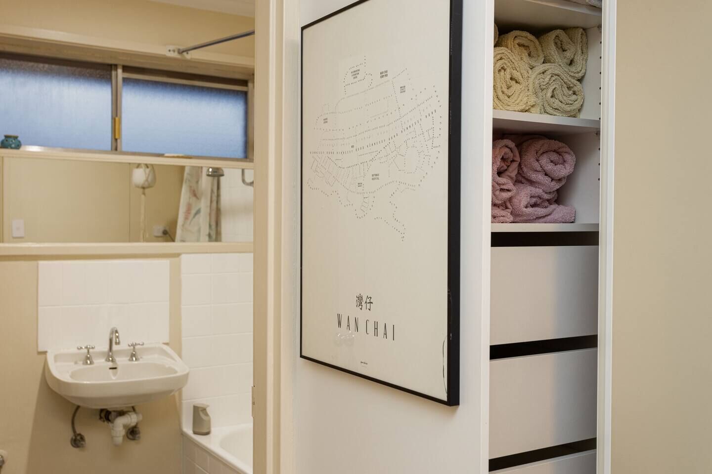 Een badkamer met een wastafel, spiegel en planken met handdoeken.