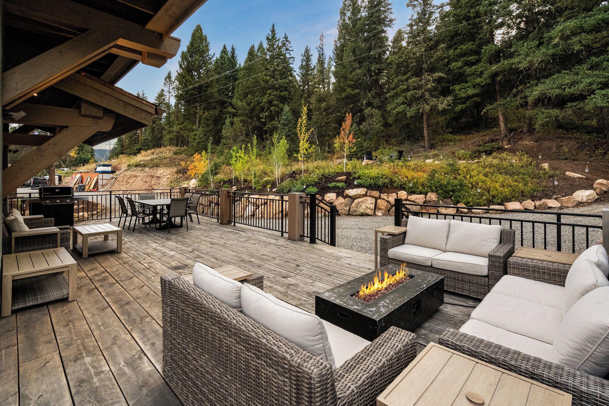 An outdoor deck with wicker furniture, a fire pit, and a view of a forested hillside.