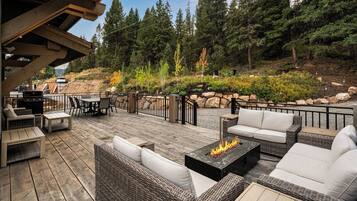 An outdoor deck with wicker furniture, a fire pit, and a view of a forested hillside.