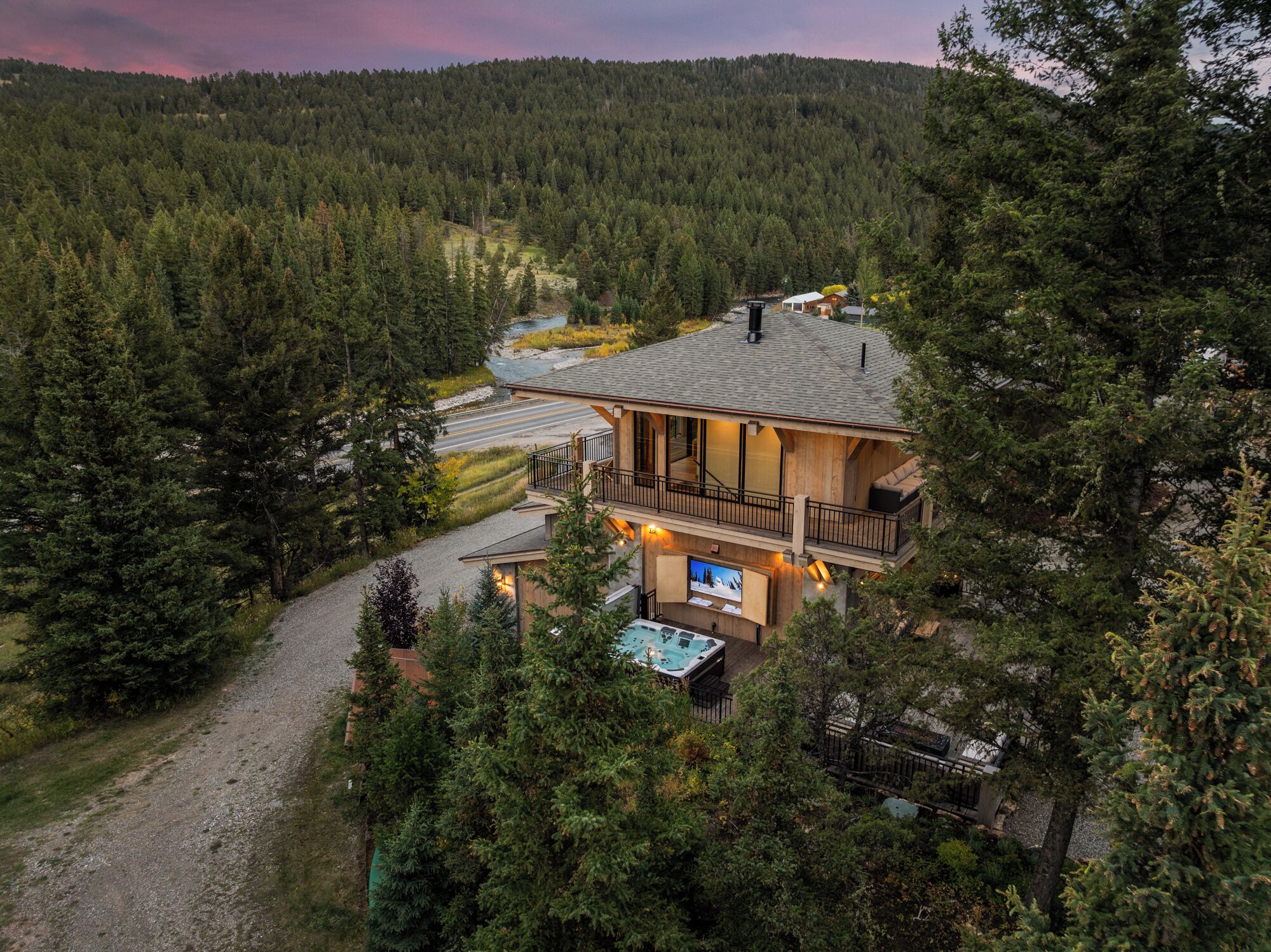 A cabin with a hot tub, surrounded by dense forest, and a road leading to it.
