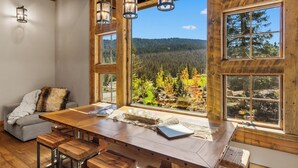 Ein Holzespeisesaal mit Bänken, große Fenster mit Blick auf einen Wald und eine gemütliche Sitzecke mit Decke und Kissen.