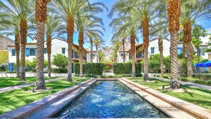 A rectangular pool with a brick border, surrounded by palm trees and a well-maintained lawn. - (L75) Newly Renovated Single Story Townhome with Gorgeous Views, sleeps 8 (La Quinta)