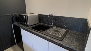 A compact kitchen with a black countertop, a microwave, a coffee maker, and a sink with a faucet. - Harden Country Club Motel (Harden)