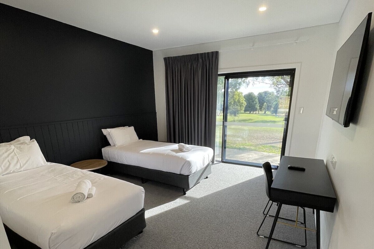 Une chambre d’hôtel moderne, dotée de deux lits, d’un bureau et d’une grande fenêtre donnant sur l’extérieur.
