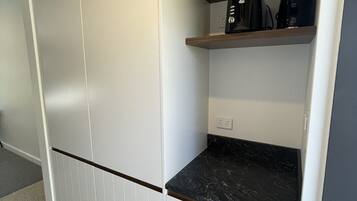 Eine Küche mit weißen Schränken, einer schwarzen Arbeitsplatte und einem Holzregal mit einer Kaffeemaschine.