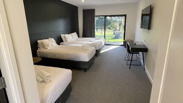 A hotel room with three beds, a desk, and a large window offering a view of the outdoors. - Harden Country Club Motel (Harden)