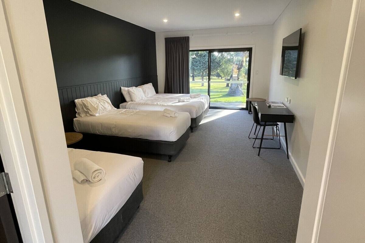 Une chambre d’hôtel avec trois lits, un bureau et une grande fenêtre donnant sur l’extérieur.