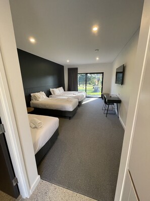 A hotel room with three beds, a desk, and a large window offering a view of the outdoors. - Harden Country Club Motel (Harden)