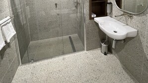 A modern bathroom with a glass-enclosed shower, a white sink, and a wooden cabinet. - Harden Country Club Motel (Harden)