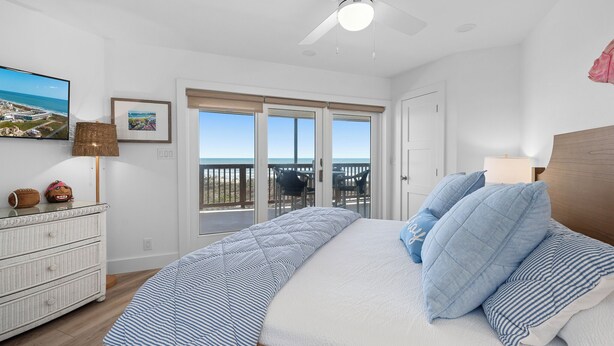 Un dormitorio con cama, cómoda, ventilador de techo, televisor y balcón con vistas.