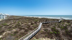 Un paseo marítimo que lleva a una playa, con vista al océano y una hilera de edificios al fondo.