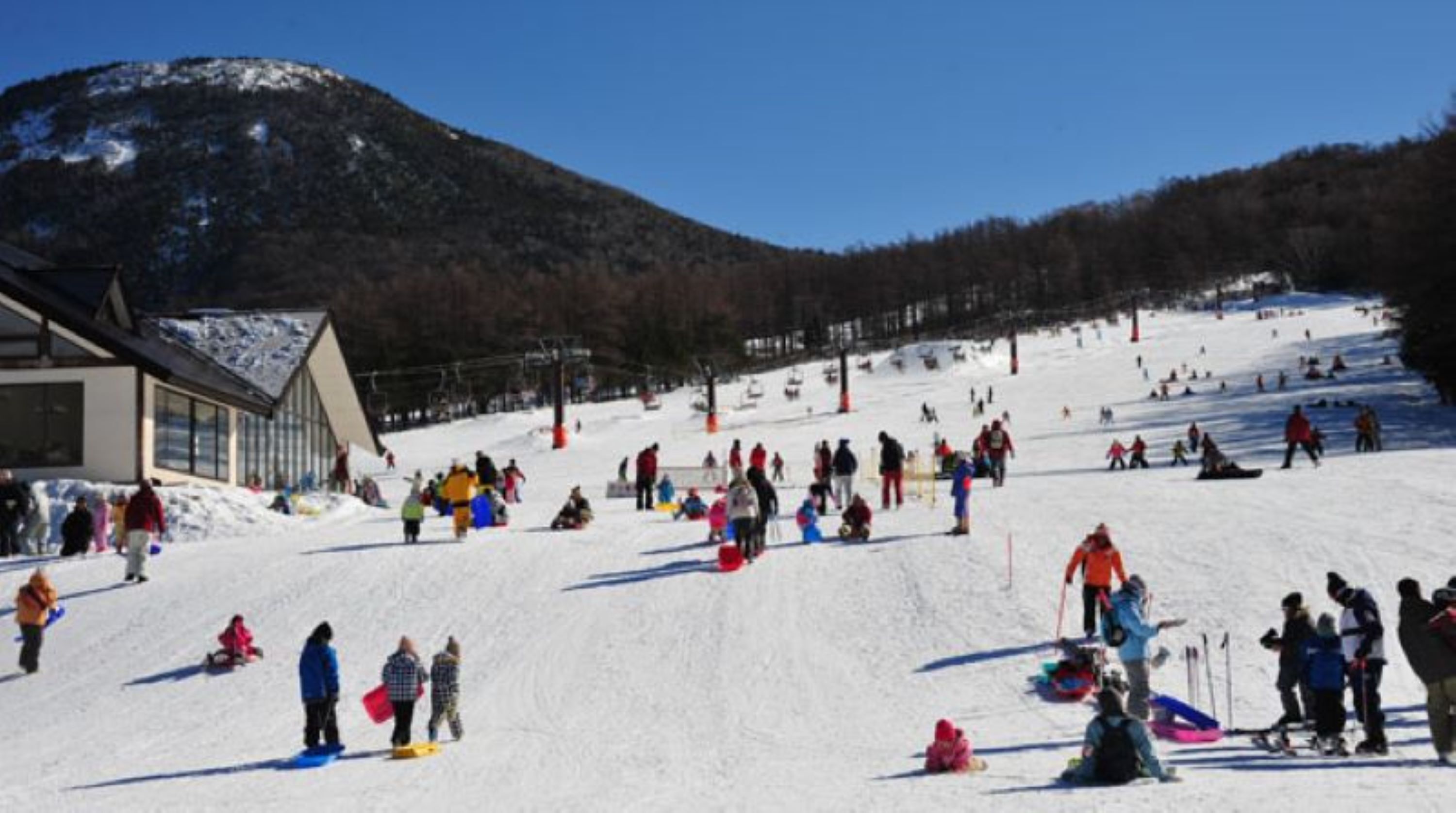 Ein Skigebiet mit einem Gebäude links, einer Skipiste und einem Berg im Hintergrund.
