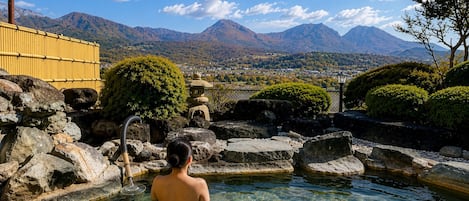 Une personne se trouve dans une piscine aux eaux cristallines, avec une vue sur la montagne, entourée de rochers et d’un jardin japonais traditionnel.