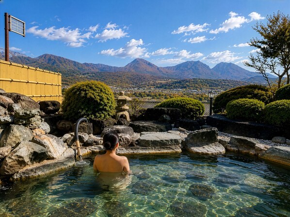 Una persona en una piscina cristalina con vista a la montaña, rodeada de rocas y jardinería tradicional japonesa.